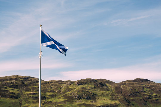the scottish flag waves in the wind with typical highland scenery in the background