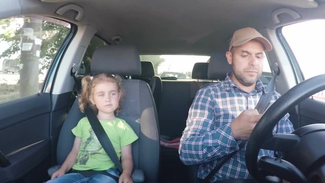 The father and his little daughter are driving in the car. A bad parent uses a smartphone while driving a car. Man texting and driving with his daughter in the car.