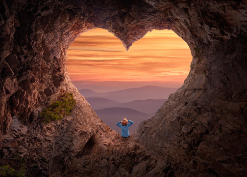 Woman in heart shape cave towards the vast landscape