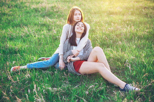 Two young women sitting on the grass field at sunset. Best friends
