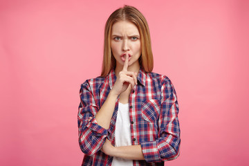Isolated shot of pretty angry woman being annoyed with loud noise, keeps fore finger on lips,...