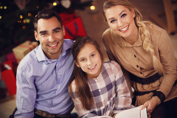 Family reading story book together under Christmas tree