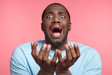 Portrait of stressful African American male has panic screams and gestures in terror, begs someone for forgiveness, doesn`t know how to prove his guiltness. Black man in despair poses indoors. - obrazy, fototapety, plakaty