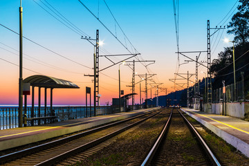 Obraz na płótnie Canvas The railway station with the illuminated platform and the railroad going into the distance at twilight, Sochi, Russia