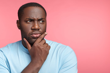 Serious dark skinned male enterpreneur dressed casually, looks thoughtfully aside, tries to create...