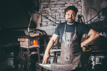 The portrait of blacksmith preparing to work metal on the anvil - obrazy, fototapety, plakaty