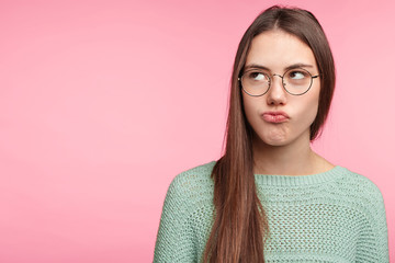 Fototapeta premium Horizontal portrait of displeased offended female pouts lips, being abused by boyfriend, has bad relationships, looks aside with discontent expression, frowns face. Facial expressions concept