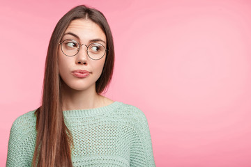 Thoughtful pensive pretty young female has long dark straight hair, dressed in knitted sweater and...