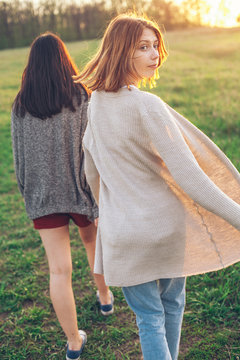 Two young women walking outdoors at sunset. One woman has turn around.
