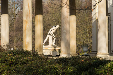 Sculpture of Gladiator by Franciszek Pinck, 1779, naked man with sword and shield among columns of the Baroque building of the Palace on the Isle in Warsaw Royal Baths Park in warm sunlight - obrazy, fototapety, plakaty