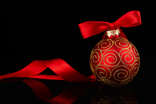 Red Christmas ball with bow on shiny reflective black background.Christmas card.New Year decoration.Holiday background with space for text.