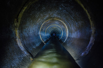 Dark underground sewer round concrete tunnel. Industrial wastewater and urban sewage flowing throw...