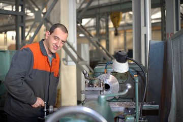 metalworking industry: factory man worker in uniform working on lathe machine in workshop
