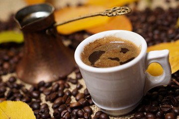 Coffee cup on sackcloth with autumn leafs and coffee beans around