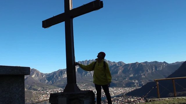 Pellegrino prega davanti a una grande croce in montagna