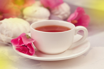 cup of tea with pink flowers on white wooden background, spring morning background. toned photo