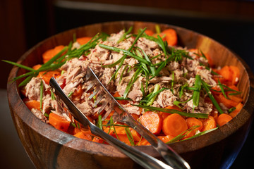 Salad with tuna, greens and carrots in a wooden bowl