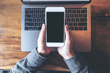 Top view mockup image of business woman holding mobile phone with blank white screen with latop on wooden table in cafe