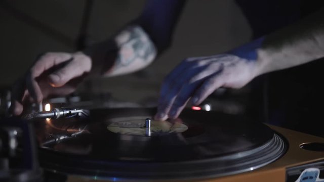 Disc jockey scratch vinyl record with music on turntable records player. Turntables vinyl disc in focus. Play music on dj audio equipment in night club. Close up,focus on djs hand on disc. Turntables