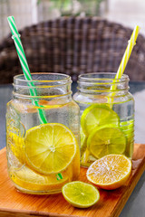 Two mason jar glasses of homemade lemonade with part of  lemons on a wooden cutting board on table background.