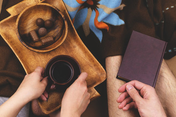 A girl and a boy at home under a blanket, drink coffee, relax