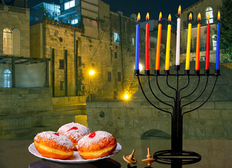 Image of jewish traditional holiday Hanukkah with menorah (traditional Candelabra), donuts and wooden dreidels (spinning top) on Jerusalem background.