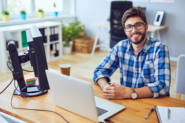 Smiling young programmer staring straight at camera while sitting at his desk