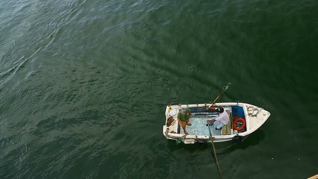 Men sailing in small boat rowing it with oars along river under bridge, top view