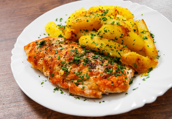 Grilled chicken breast with potato in a plate on a wooden background.
