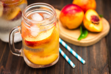 Mason jar glass of homemade peach iced water on a rustic wooden background.