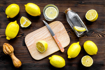 Prepare refreshing beverage lemonade. Lemons, juicer, bottle, knife, cutting board on dark wooden background top view