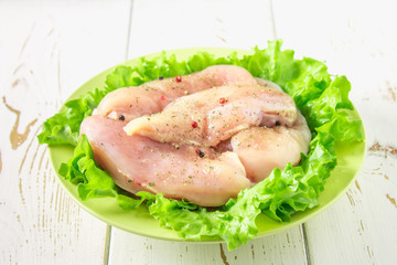 Raw chicken fillet and green salad in a yellow bowl on a white wooden table. Meat ingredients for cooking. Top view.