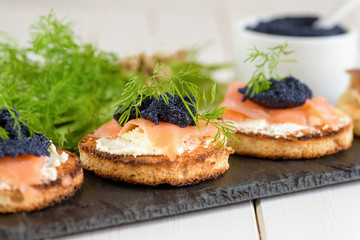 Appetizer toast bread with cream cheese, smoked salmon and black caviar decorated by dill.