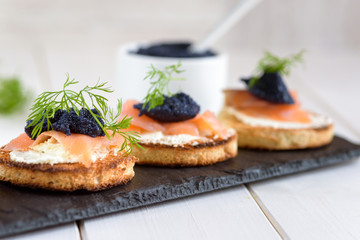Appetizer toast bread with cream cheese, smoked salmon and black caviar decorated by dill.
