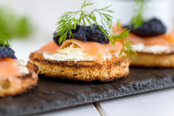 Appetizer toast bread with cream cheese, smoked salmon and black caviar decorated by dill.