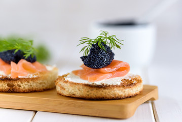 Appetizer toast bread with cream cheese, smoked salmon and black caviar decorated by dill.