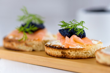 Appetizer toast bread with cream cheese, smoked salmon and black caviar decorated by dill.
