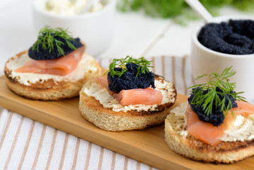 Appetizer toast bread with cream cheese, smoked salmon and black caviar decorated by dill.