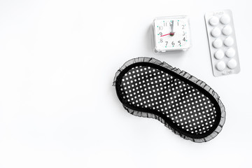 Sleeping pills for insomnia near sleep mask and alarm clock on white background top view copyspace