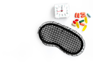 Sleeping pills for insomnia near sleep mask and alarm clock on white background top view copyspace