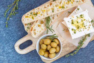 Green olives, feta cheese and fresh ciabata on a wooden board