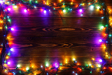 Wreath and garlands of colored light bulbs.Christmas background with lights and free text space. Christmas lights border. Glowing colorful Christmas lights on a wooden background. New Year.  