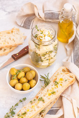 Green olives, feta cheese with olive oil in a jar and fresh ciabatta