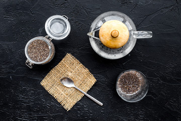 Obraz na płótnie Canvas Brew chia seeds. Jar with seeds, scoop, bowl, tea pot with hot water. Black background top view