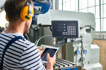 Back view portrait of young factory worker operating machine units at modern factory using digital tablet with electronic control, copy space