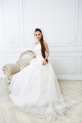 Slim beautiful young woman posing in a wedding dress in studio. Looks at a camera