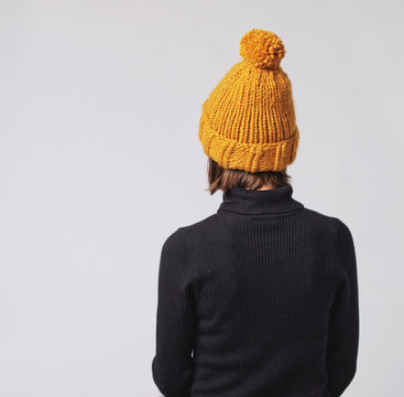 Woman wearing mustard knit beanie hat with big pom pom and black turtleneck isolated on grey background. Copy space