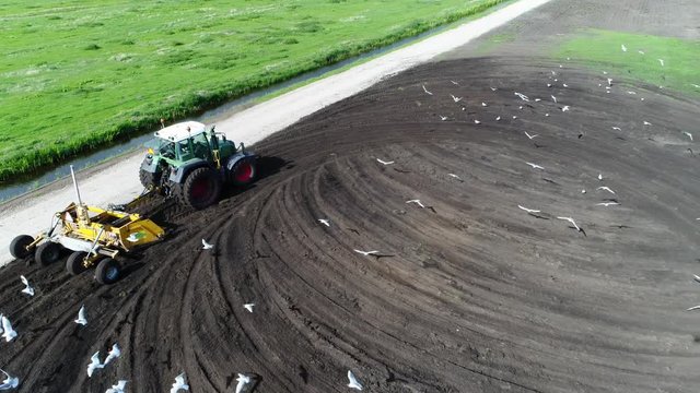 Aerial footage of tractor plowing land for initial cultivation of soil in preparation for sowing seed or planting to loosen or turn the soil stable footage also showing sea gull looking for food 4k