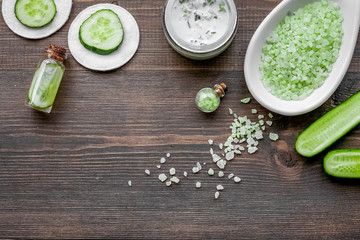 Natural cucumber cosmetics. Lotion, cream, spa salt on dark wooden background top view copyspace
