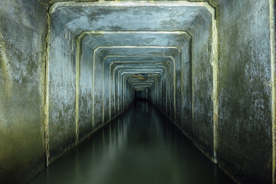 Dark and creepy flooded underground sewer concrete tunnel. Industrial wastewater and urban sewage flowing throw the tunnel